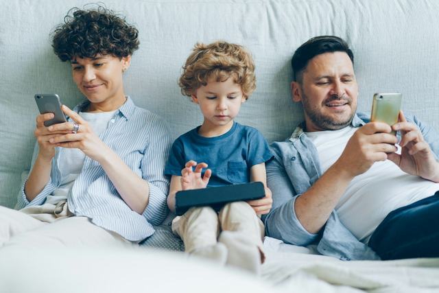A family relaxing on a sofa with phones and a tablet